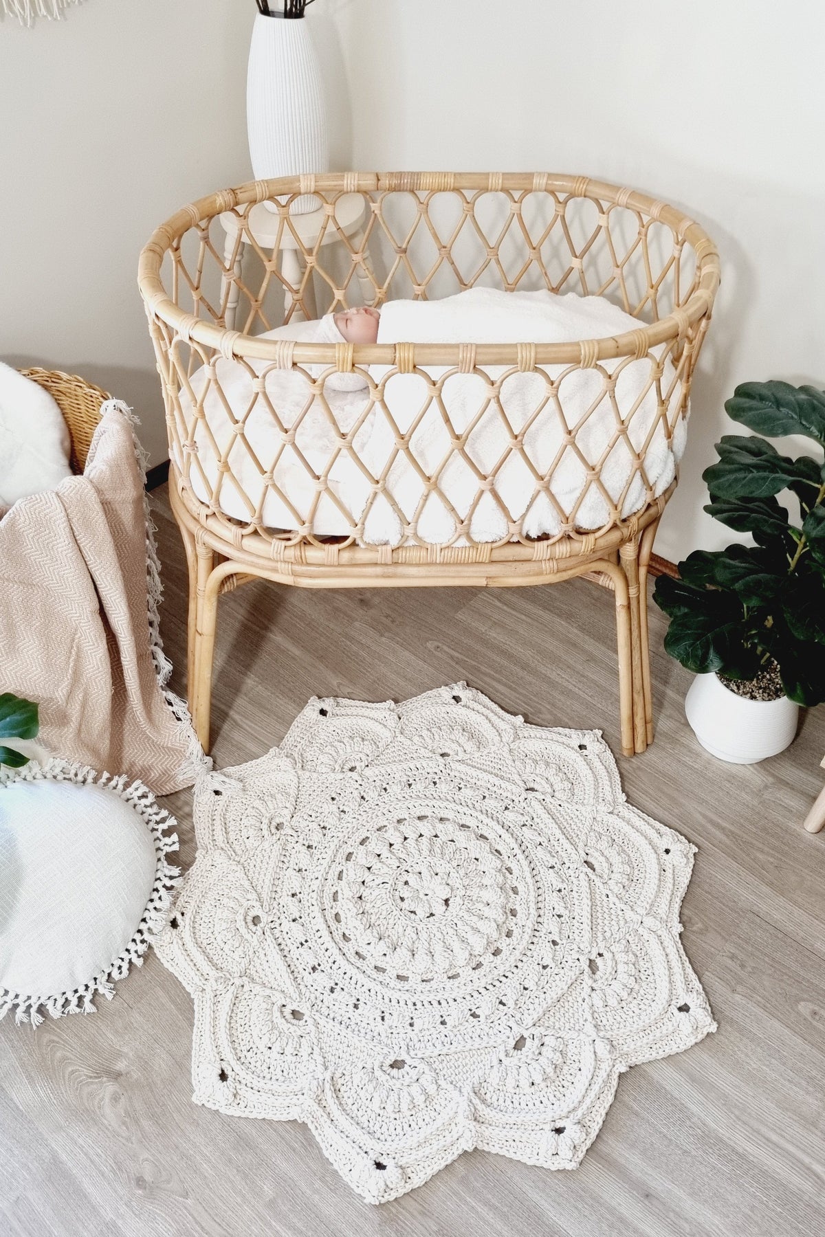 White crocheted floor rug in the shape of a flower on the floor in front of a ratten bassinet.