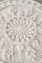 Close-up of a cream-colored crocheted textile with a raised circular floral or sunburst motif and textured crochet details.