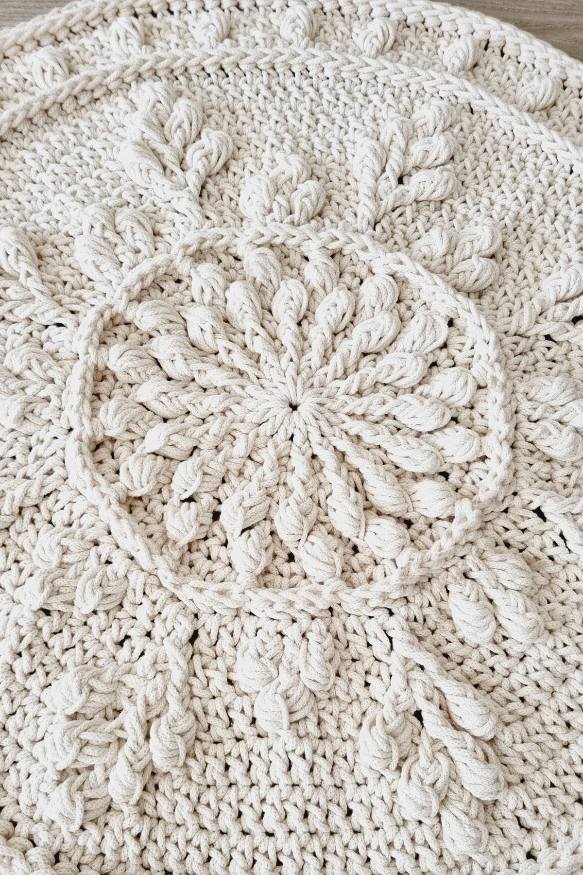 Close-up of a cream-colored crocheted textile with a raised circular floral or sunburst motif and textured crochet details.