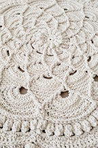 Close-up of a round crocheted textile with an intricate lace-like floral pattern in a warm off-white or cream color.