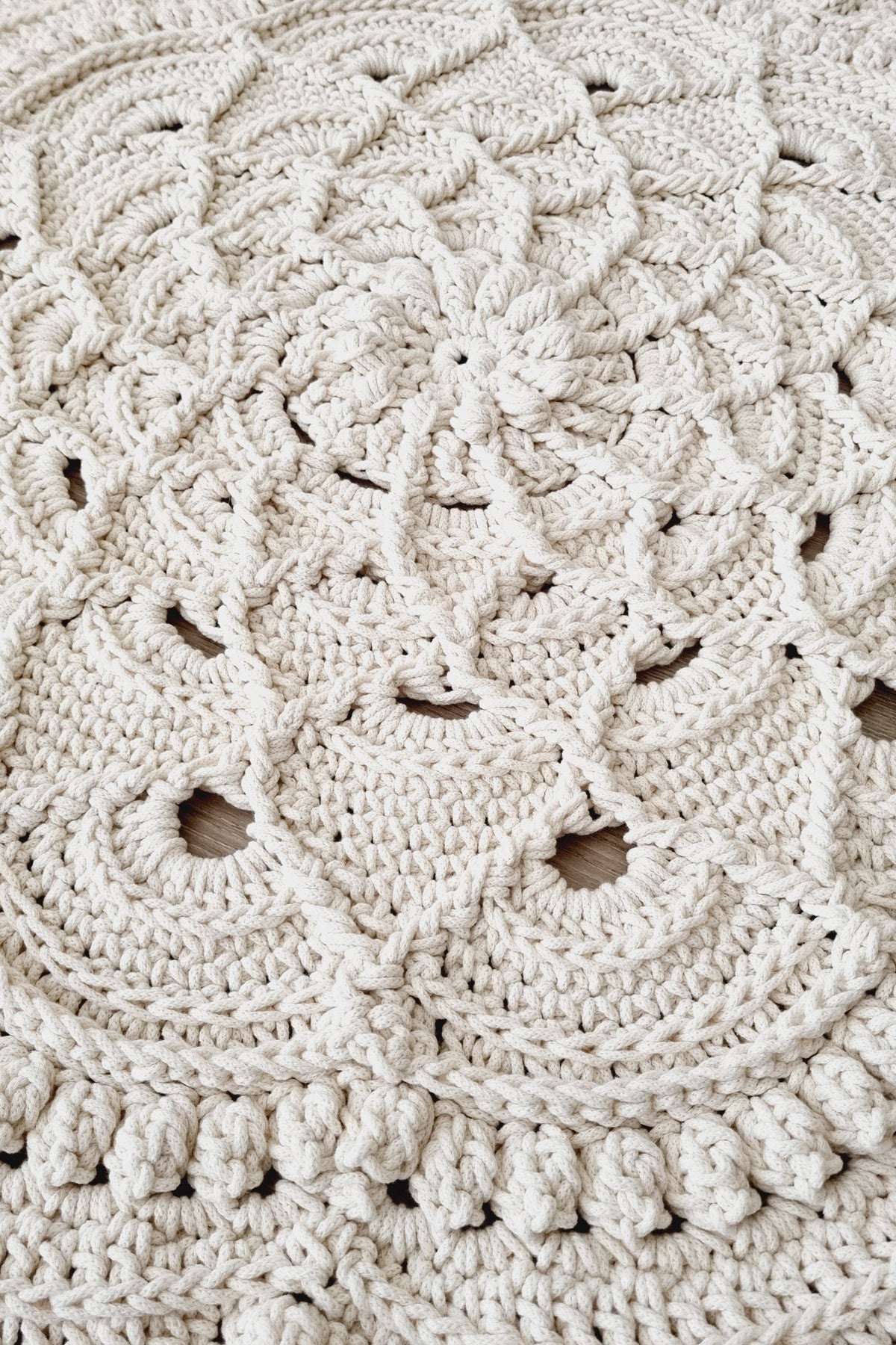 Close-up of a round crocheted textile with an intricate lace-like floral pattern in a warm off-white or cream color.
