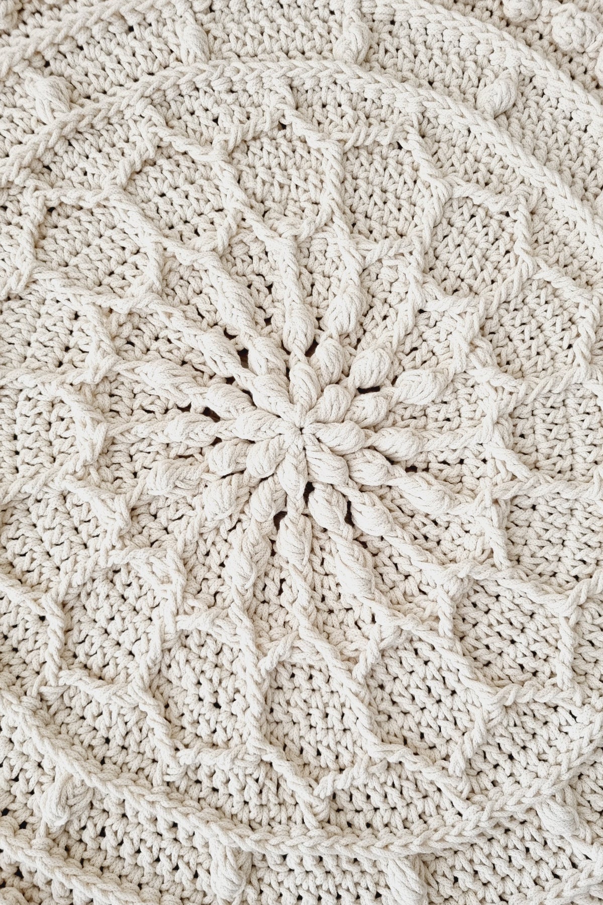 Close-up of a cream-colored crocheted textile with a detailed radial floral or mandala pattern, showing the texture and stitch details.