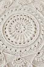 A close-up of a hand-crocheted round rug in a warm cream or off-white color, showcasing intricate circular and scalloped patterns on a light wood floor.