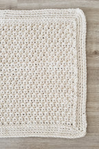 A crochet-textured floor rug in a warm cream colour, laid flat on a light grey wood floor.