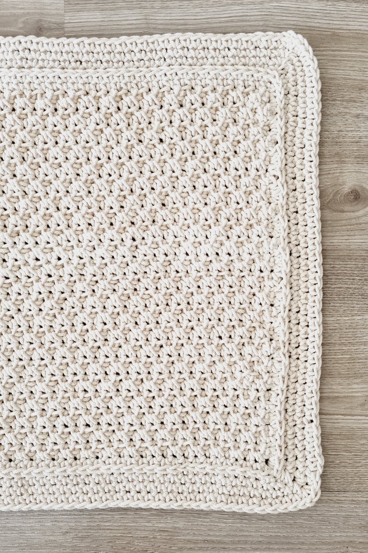 A crochet-textured floor rug in a warm cream colour, laid flat on a light grey wood floor.