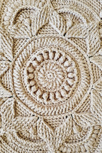 Close-up of a brown crochet floor rug with an intricate circular mandala pattern and textured stitches.