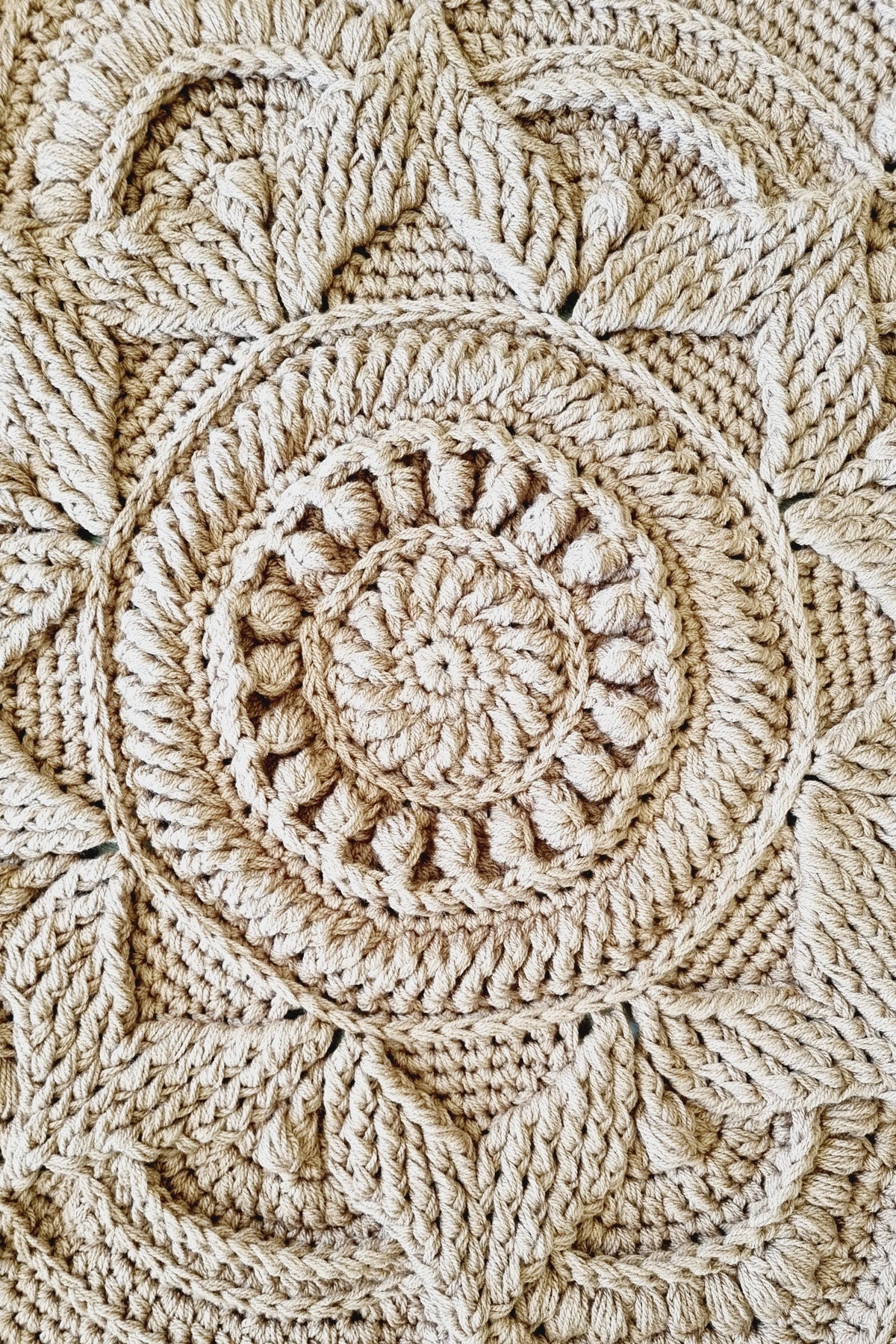 Close-up of a brown crochet floor rug with an intricate circular mandala pattern and textured stitches.