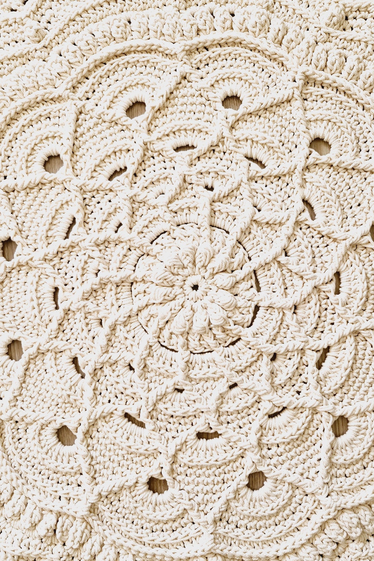 A close-up of a cream-colored crocheted floor rug with an intricate floral and scalloped lace pattern.