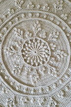 A close-up of a round crocheted floor rug with concentric circular patterns and leaf-like motifs.