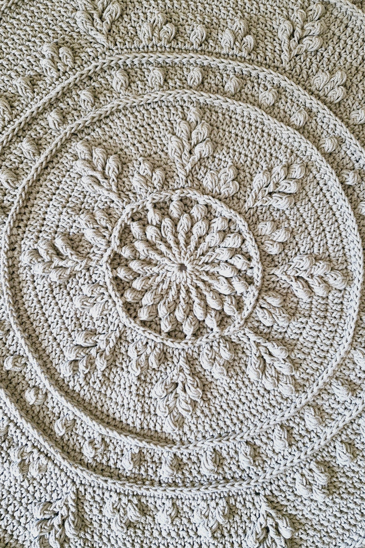 A close-up of a round crocheted floor rug with concentric circular patterns and leaf-like motifs.