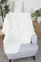 A white crochet blanket made up of hexagons with a snowflake design laid over a grey chair.