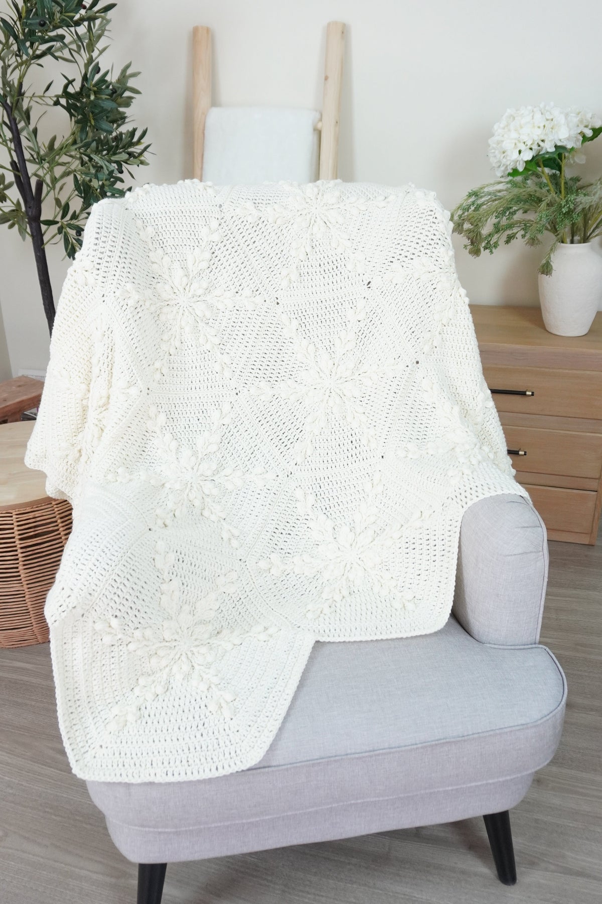 A white crochet blanket made up of hexagons with a snowflake design laid over a grey chair.