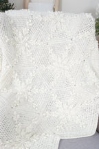 An off-white crocheted blanket with a snowflake design draped over a light gray sofa in a home setting.