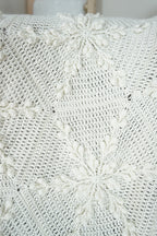 Close-up of a white crocheted blanket with textured snowflake design draped over a chair.