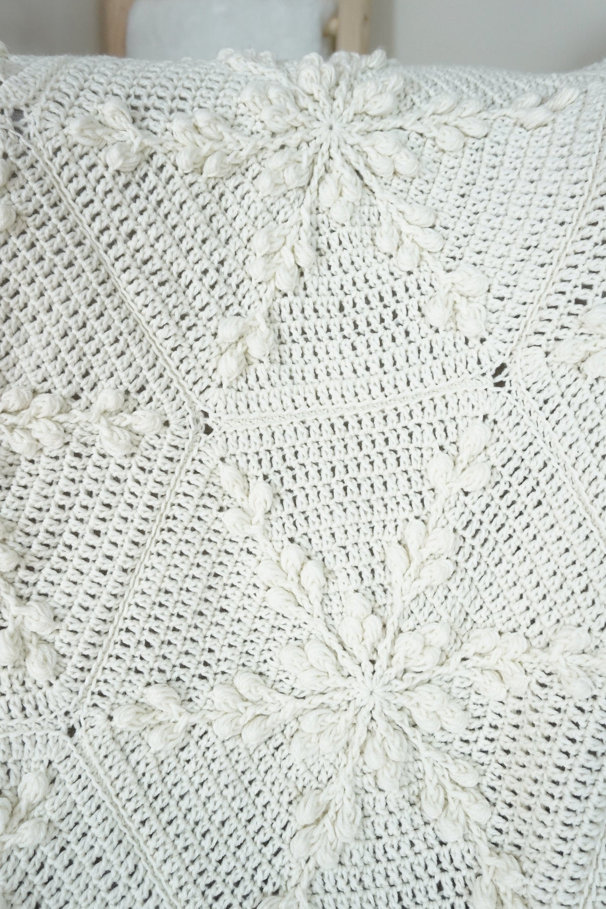 Close-up of a white crocheted blanket with textured snowflake design draped over a chair.
