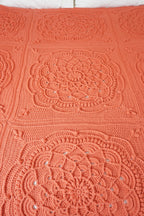 A close-up of a crocheted blanket featuring large square panels with intricate circular lace-like medallion patterns in a warm coral-orange color.