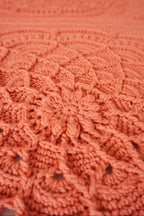 Close-up of a textured crocheted blanket in a warm coral-orange color, showing detailed floral patterns.