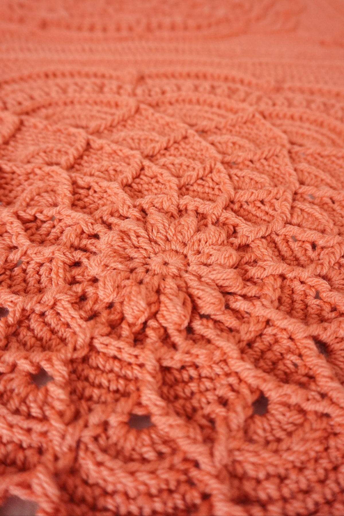 Close-up of a textured crocheted blanket in a warm coral-orange color, showing detailed floral patterns.
