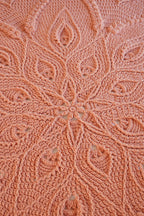 Close-up of a peach-colored crocheted blanket with an intricate floral and leaf lace pattern.