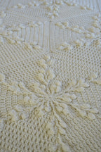 Close-up of a cream-colored crocheted blanket with snowflake motifs.