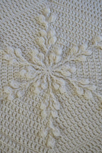 Close-up of a cream-colored crocheted blanket with a raised snowflake pattern and textured crocheted background.