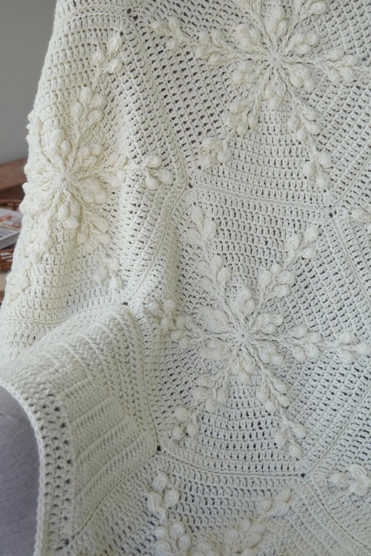 A close-up of a cream-colored crocheted blanket with textured snowflake pattern draped over a chair.