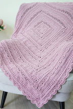 A dusty pink crocheted lace throw blanket draped over a light gray upholstered armchair with black legs, set against a neutral wall and light wood floor.