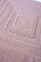 A close-up of a handmade pink crochet blanket with concentric square patterns and scalloped edges.