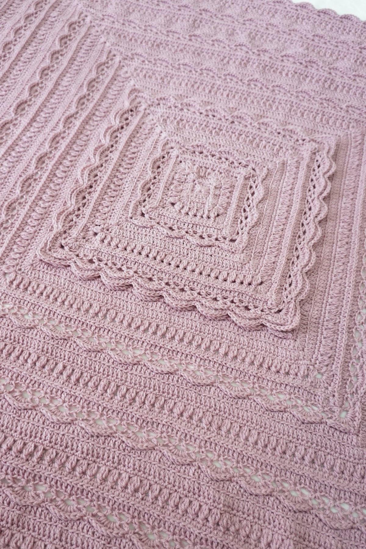A close-up of a handmade pink crochet blanket with concentric square patterns and scalloped edges.