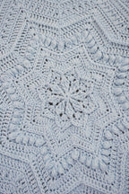 A close-up of a light blue crocheted blanket with an intricate starburst and geometric pattern.