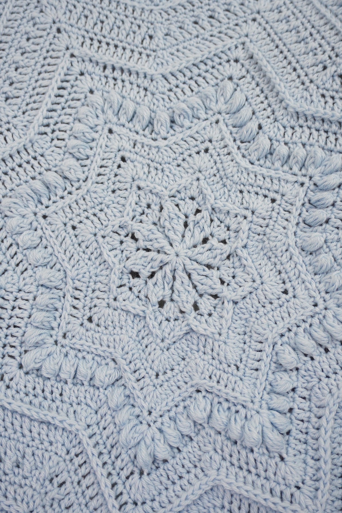 A close-up of a light blue crocheted blanket with an intricate starburst and geometric pattern.