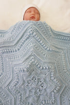 A sleeping newborn baby wrapped in a light blue crocheted blanket with a matching white hat, lying on a soft white background.