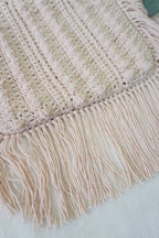 Close-up of a cream coloured crochet bag, featuring a ribbed texture and long fringe along one edge.